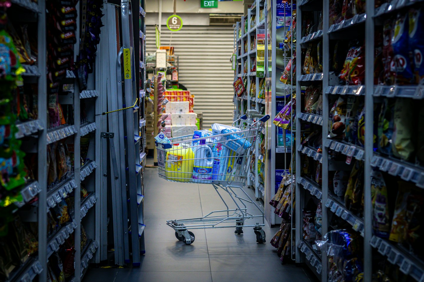 Shopping cart filled with cleaning supplies in a supermarket aisle.