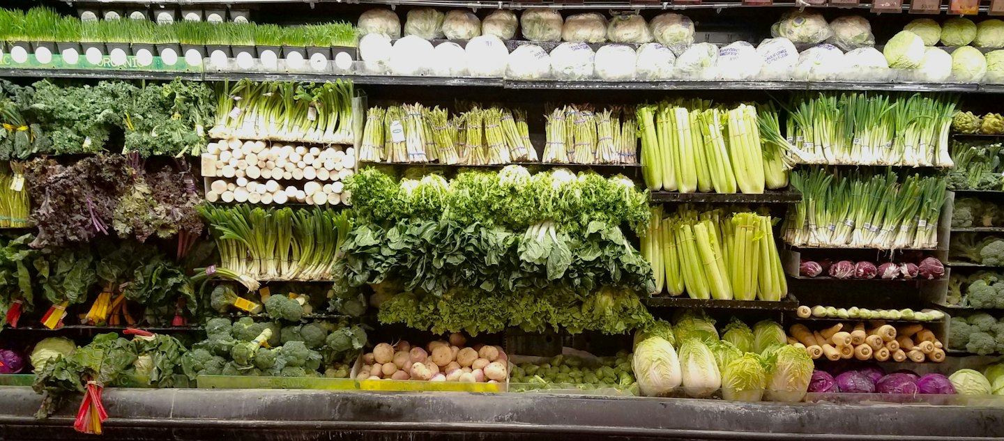 Fresh green vegetables displayed on shelves in a grocery store.